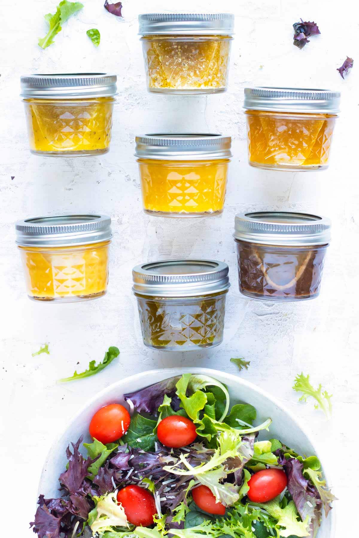 Seven healthy apple cider vinegar salad dressing recipes in mason jar containers next to a spinach and arugula salad.