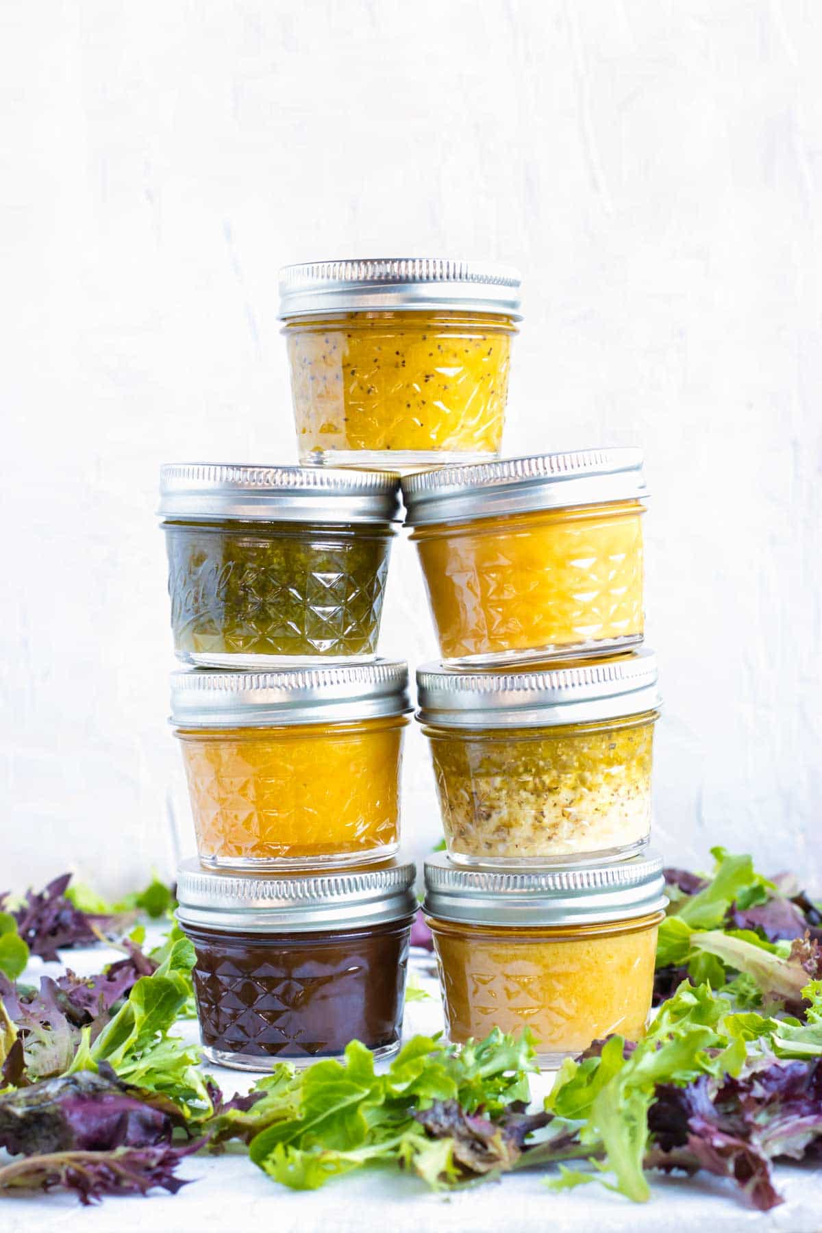 Second mason jars full of homemade salad dressing recipes in a stack with mixed greens around them.