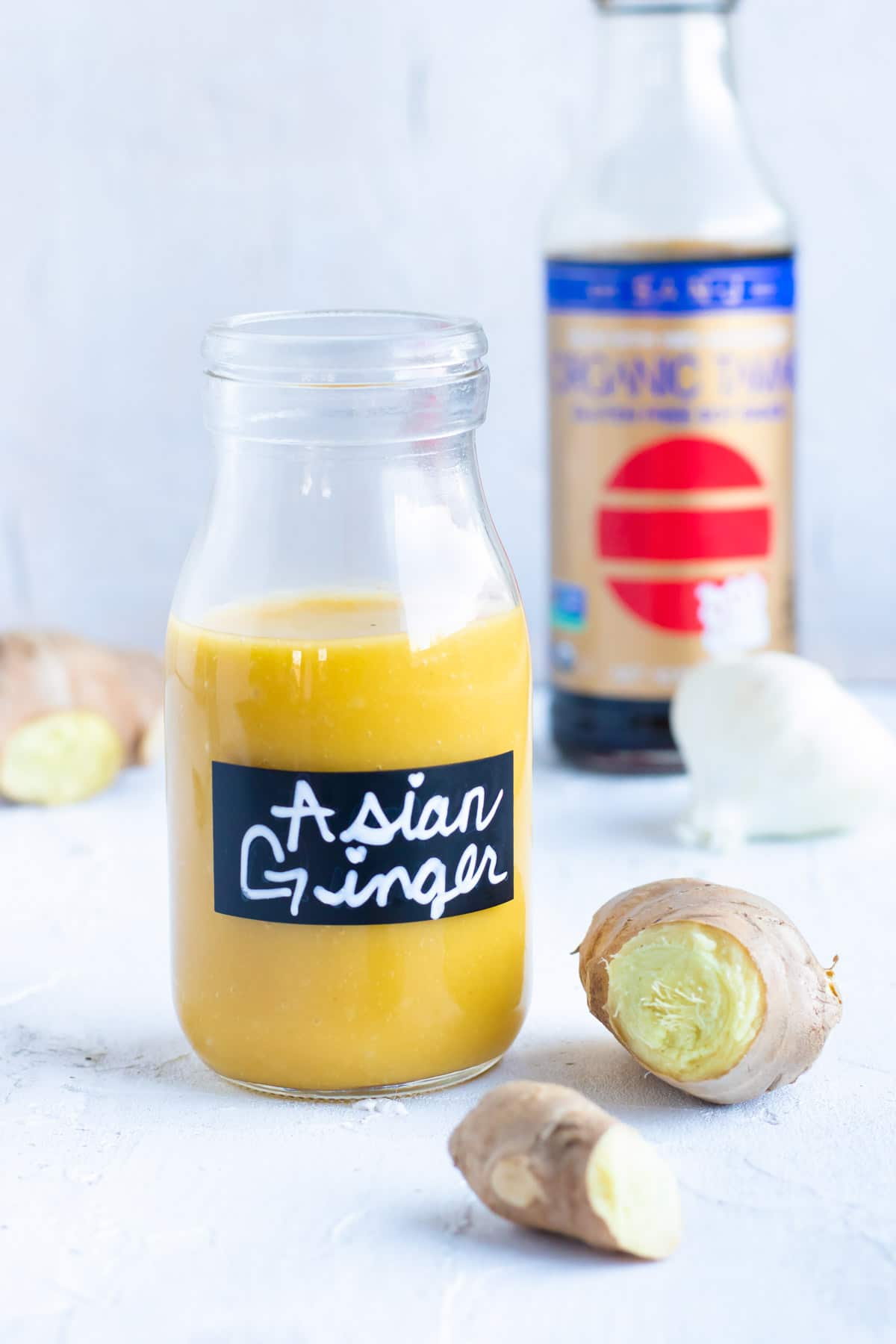 Asian Ginger salad dressing in a clear glass jar with fresh ginger and garlic next to it.