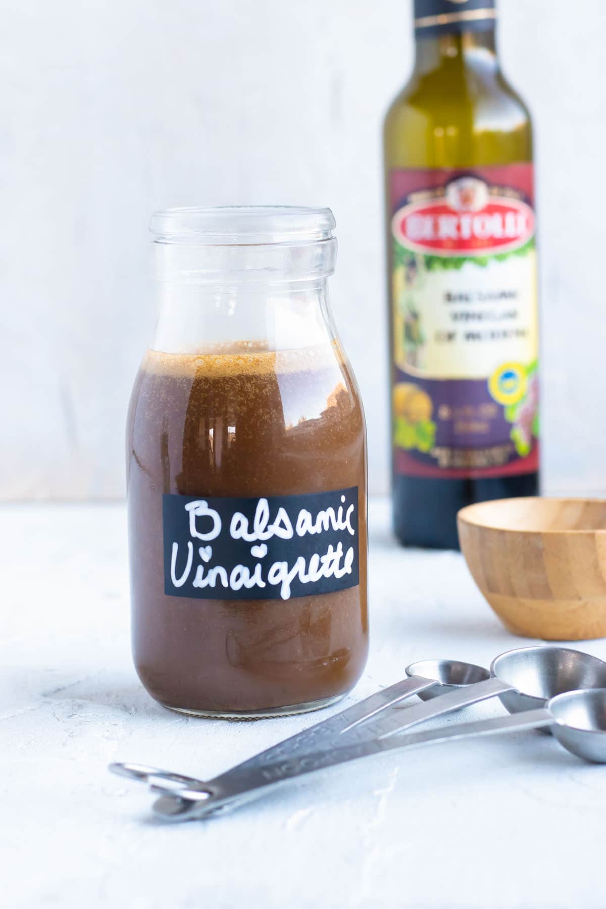Balsamic vinaigrette salad dressing in a clear glass jar with balsamic vinegar in the background.