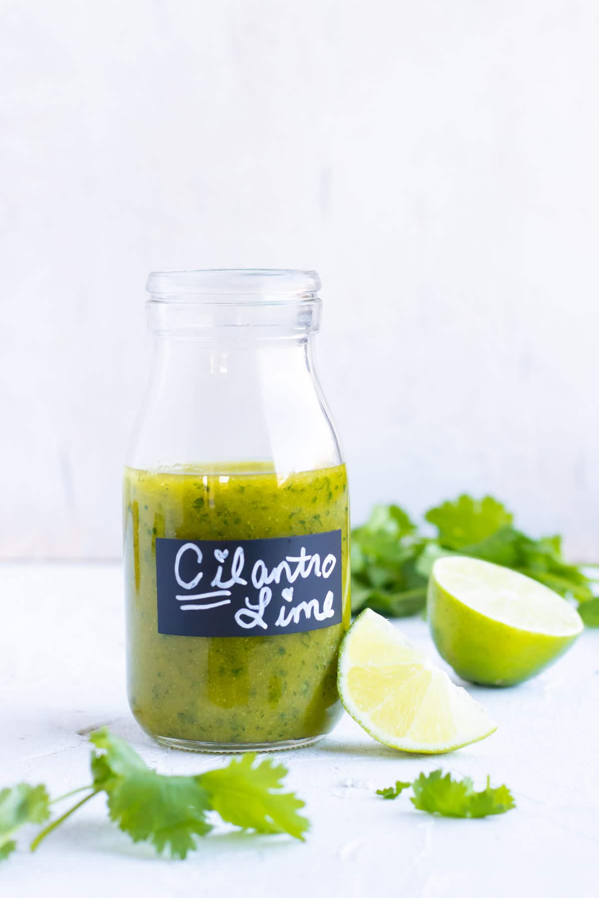 Cilantro lime vinaigrette dressing in a clear glass jar with limes and cilantro next to it.