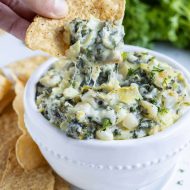 A chip is loaded with hot spinach artichoke dip for an appetizer.