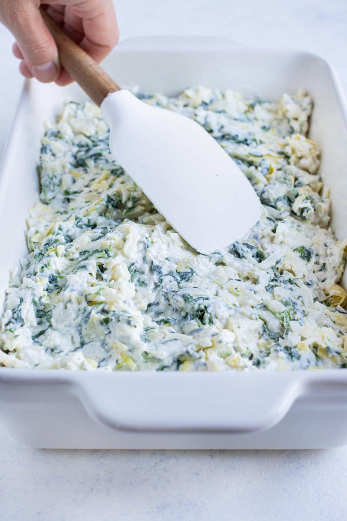 The spinach artichoke dip is spread into a baking dish.