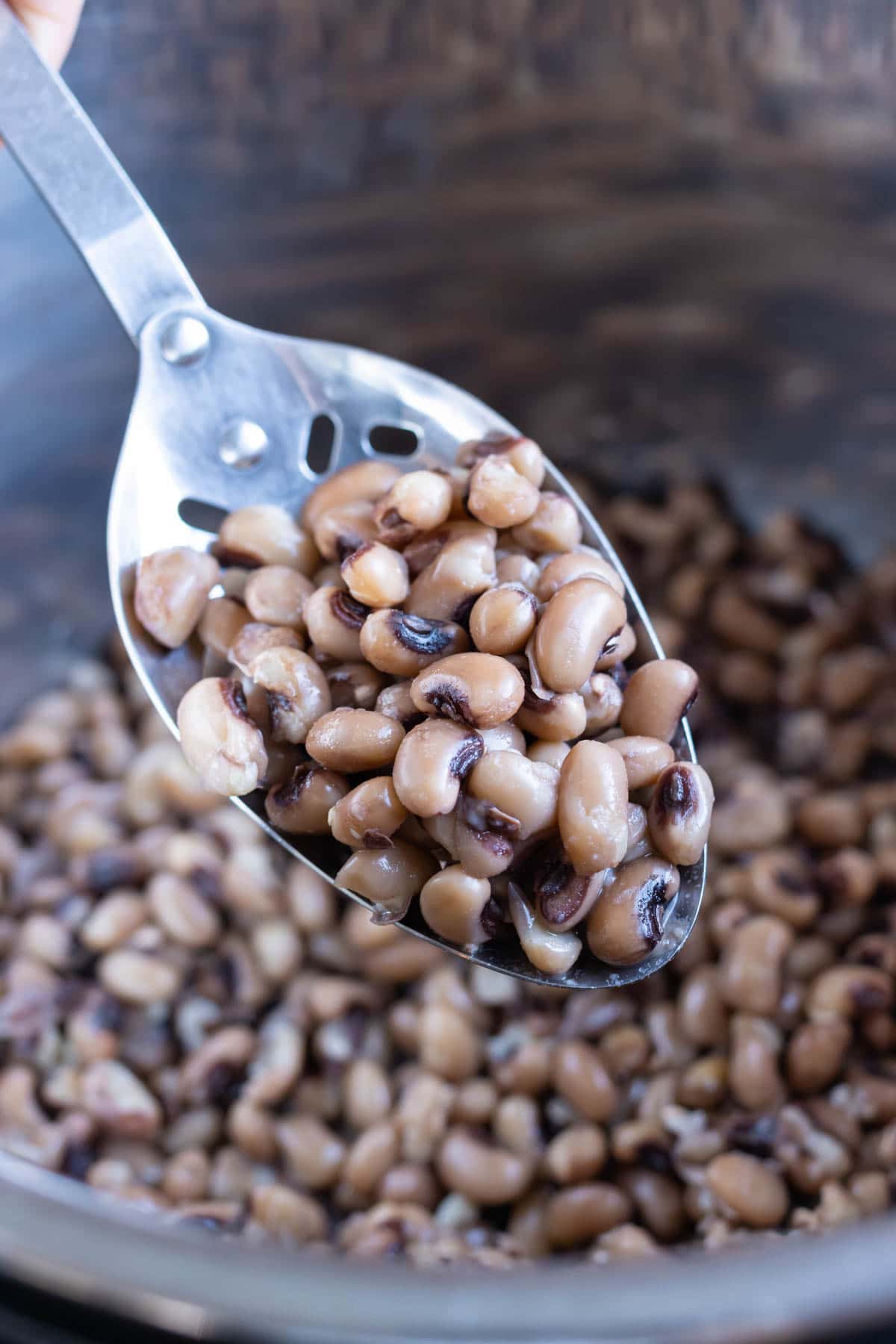 A slotted spoon is shown removing black eyed peas from the instant pot.