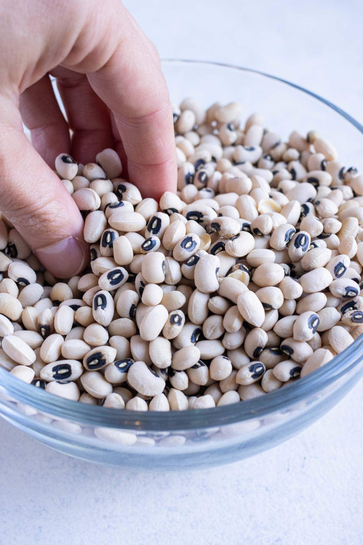 Hands are holding dry black eyed peas in a bowl.