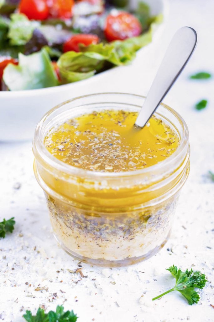 A small glass jar full of a homemade Italian dressing recipe is shaken up.