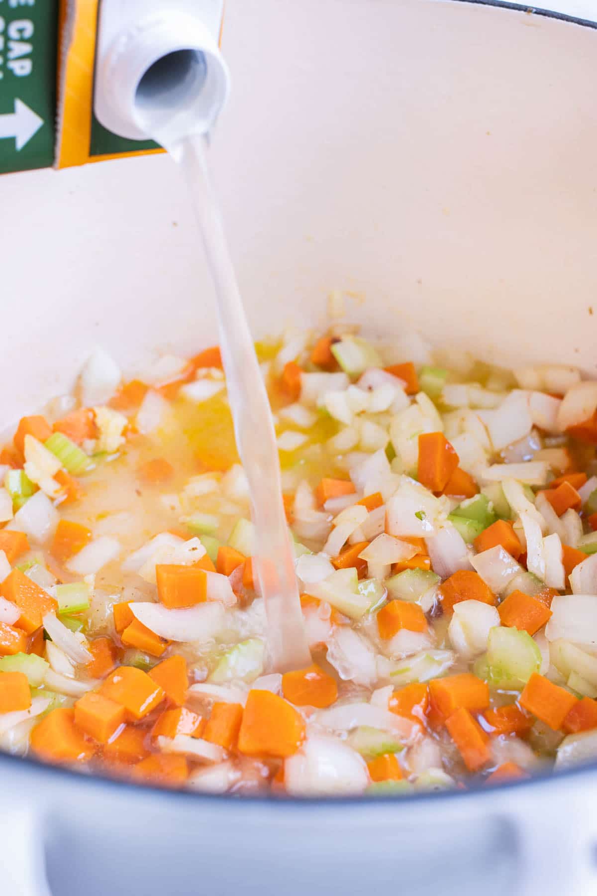 Broth is added to the vegetables in a pot.