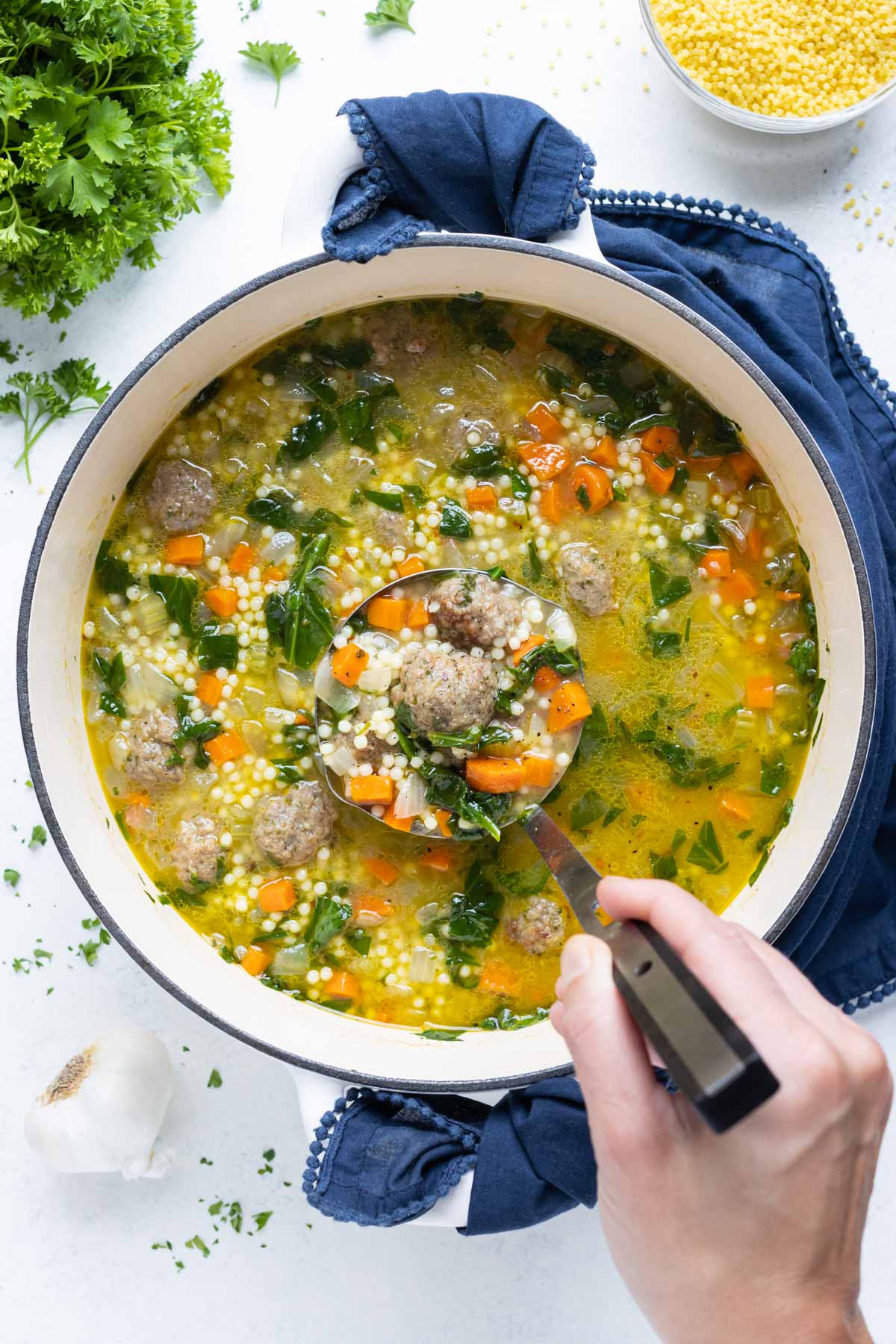 A big pot of Italian wedding soup is served with a ladle.