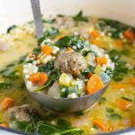 A ladle is shown full of comforting Italian wedding soup.
