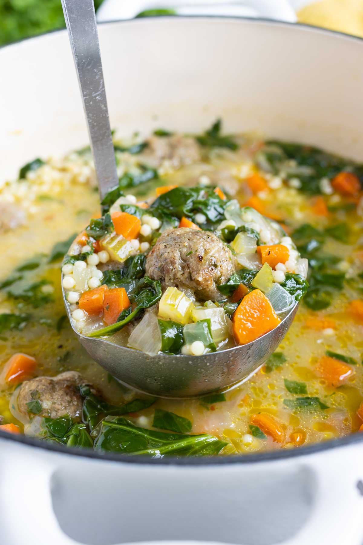 A ladle is shown full of comforting Italian wedding soup.