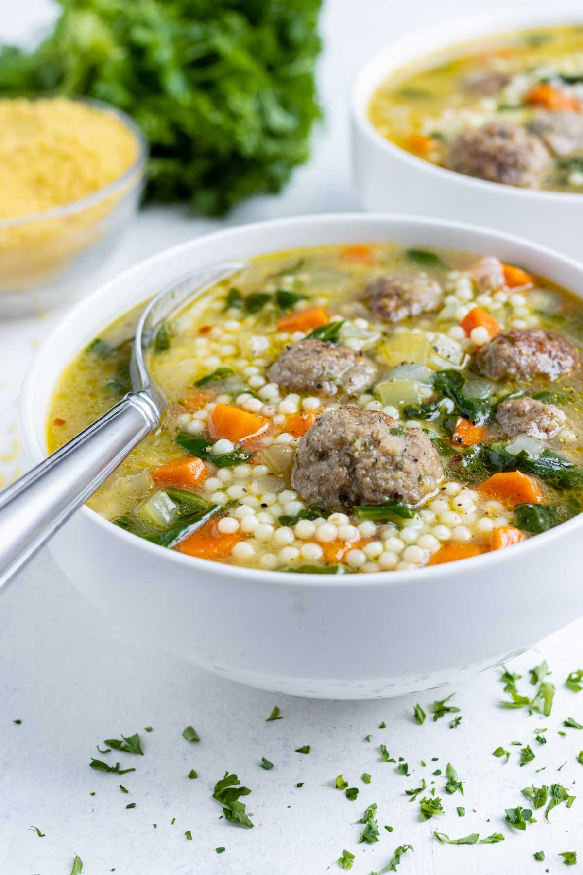 Italian wedding soup is served in a white bowl.