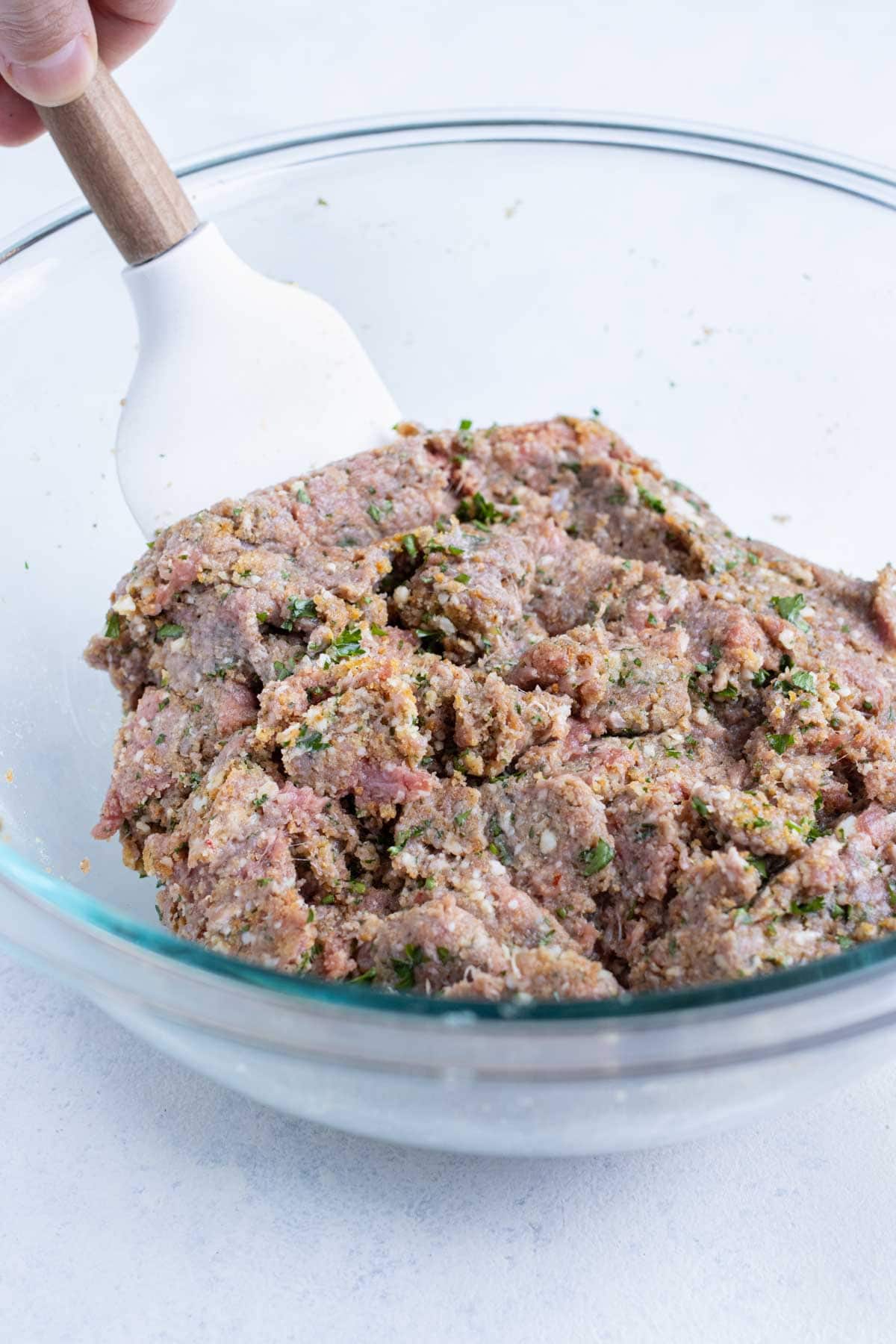 Meatball ingredients are combined in a glass bowl.