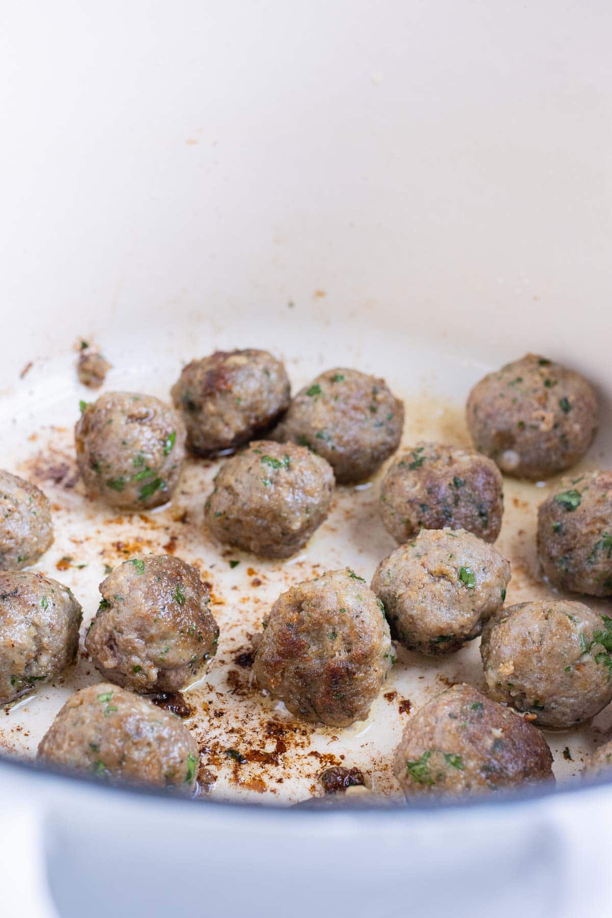 Meatballs are seared in a pan on the stove.