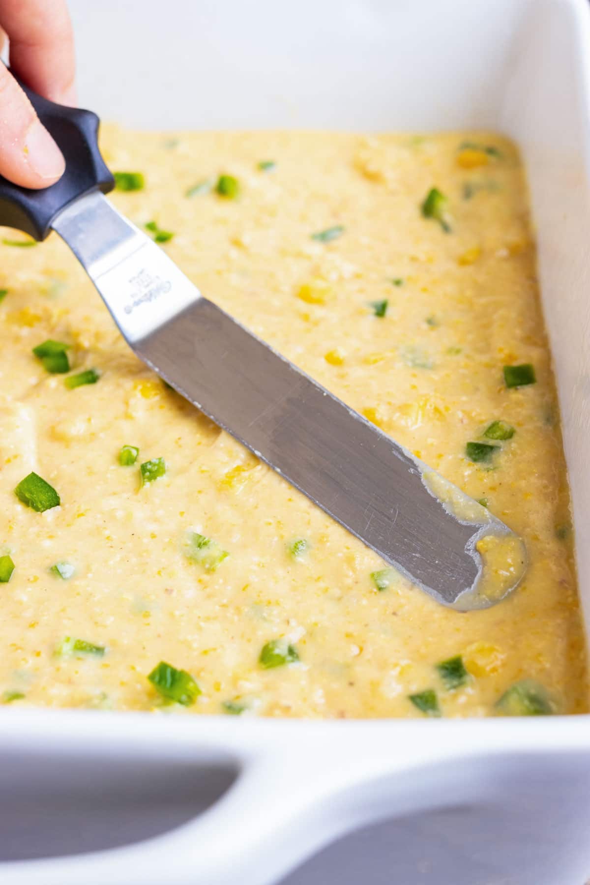 Spreading out a jalapeño cornbread batter into a large baking dish before cooking in oven.