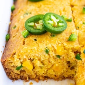 Slices of a quick and easy cornbread recipe with jalapenos, honey, and corn in a white baking dish.
