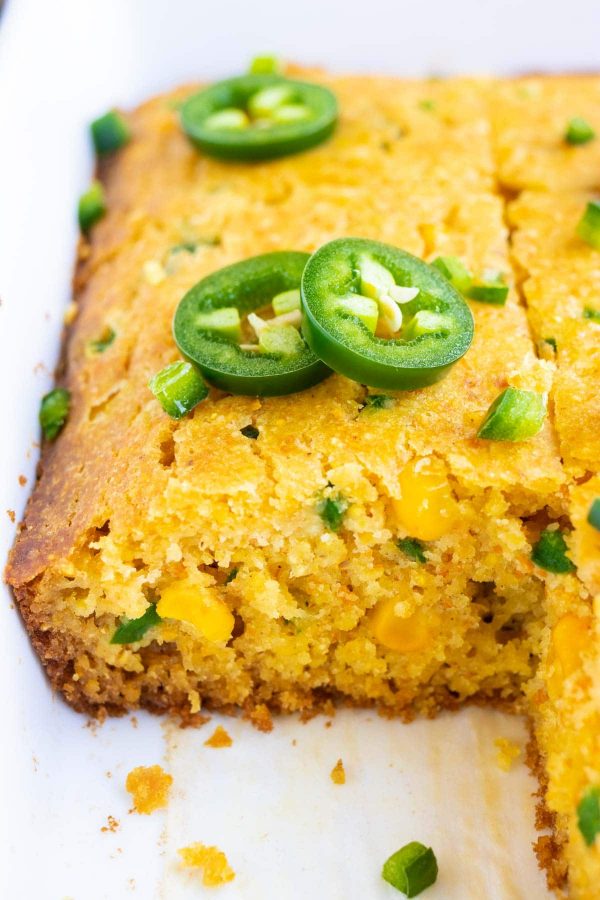 Slices of a quick and easy cornbread recipe with jalapenos, honey, and corn in a white baking dish.