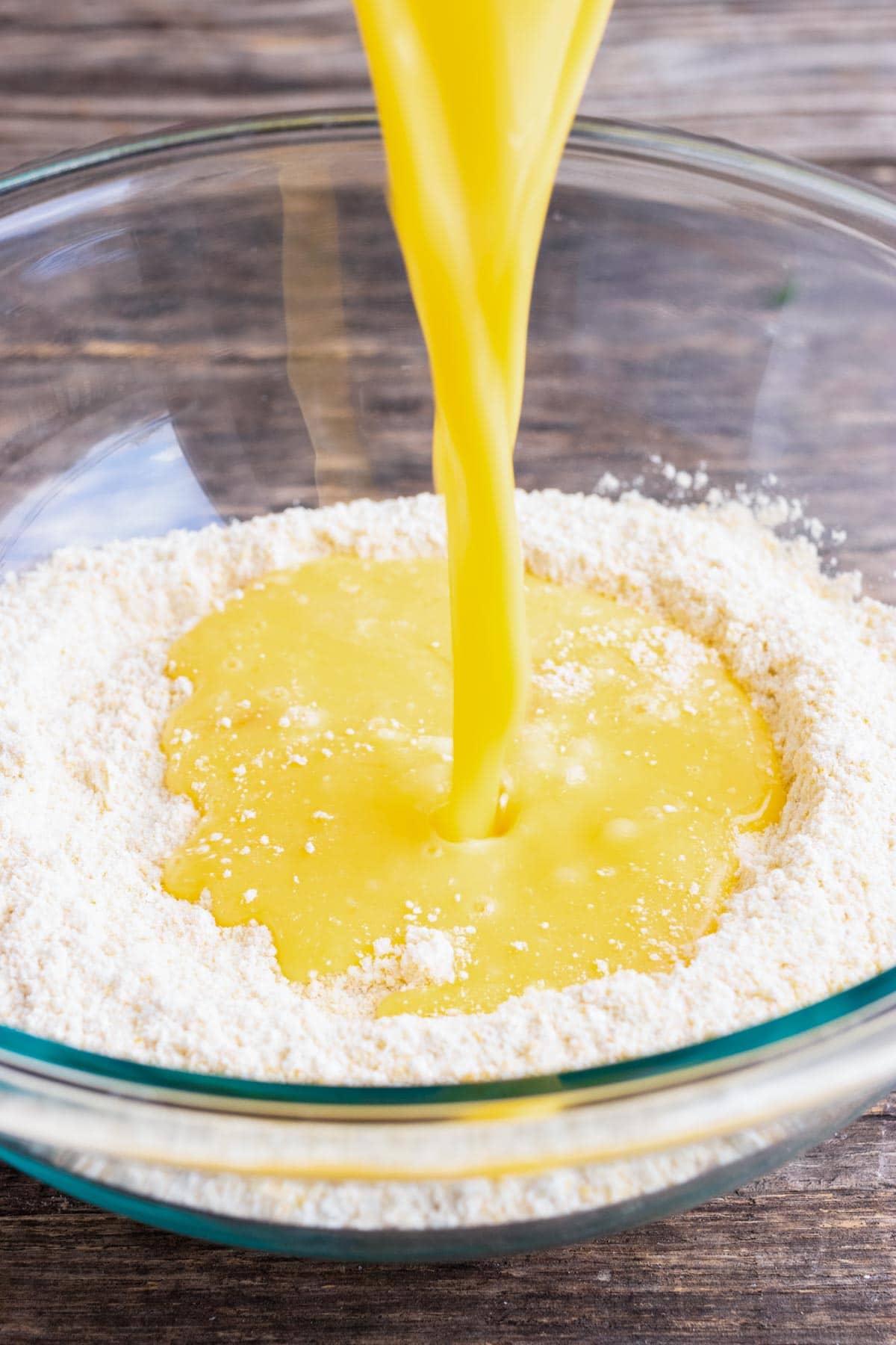 Wet ingredients being poured into dry in a glass bowl for a honey cornbread recipe.