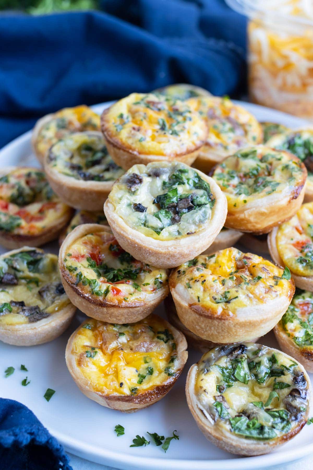 Mini quiches are piled on a white plate for serving.