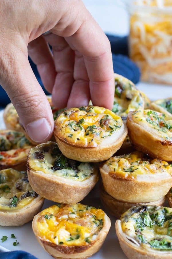 A mini quiche is picked up by a hand from a plate.