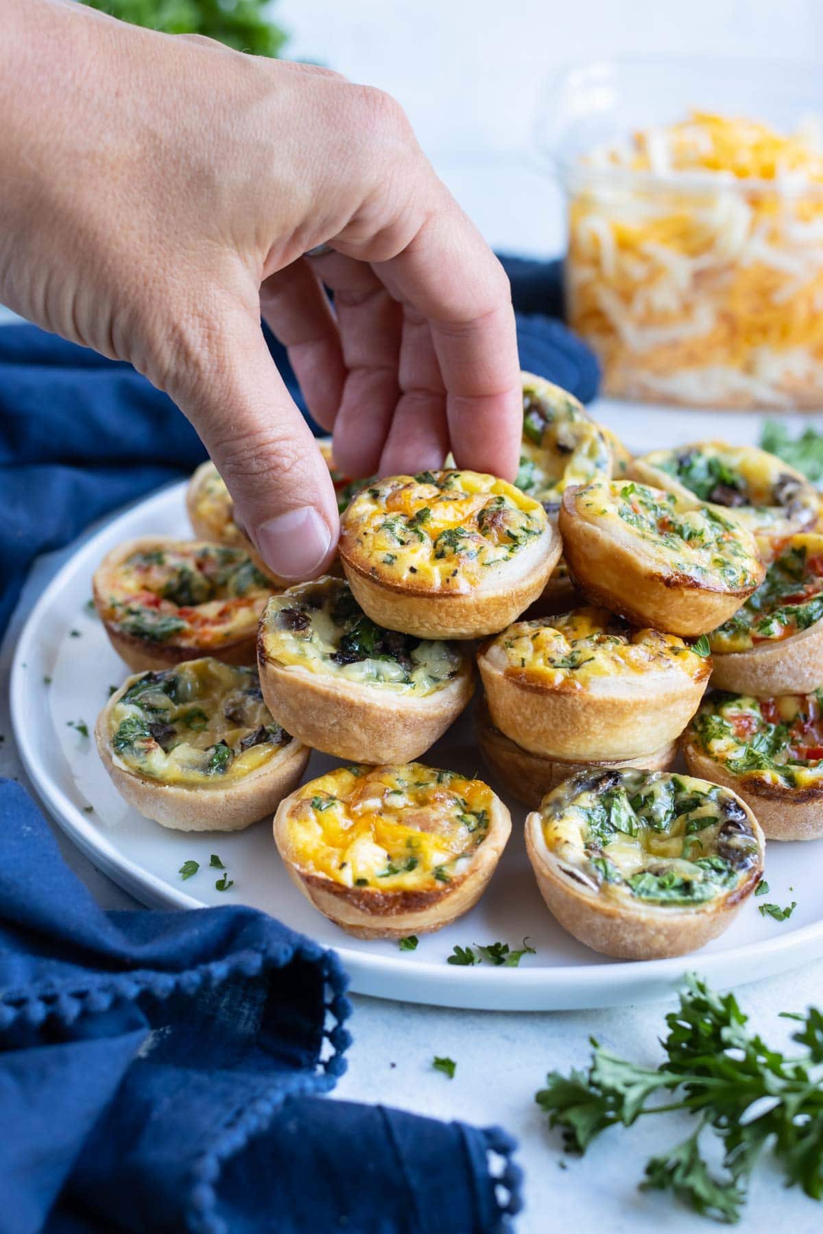 A mini quiche is picked up by a hand from a plate.
