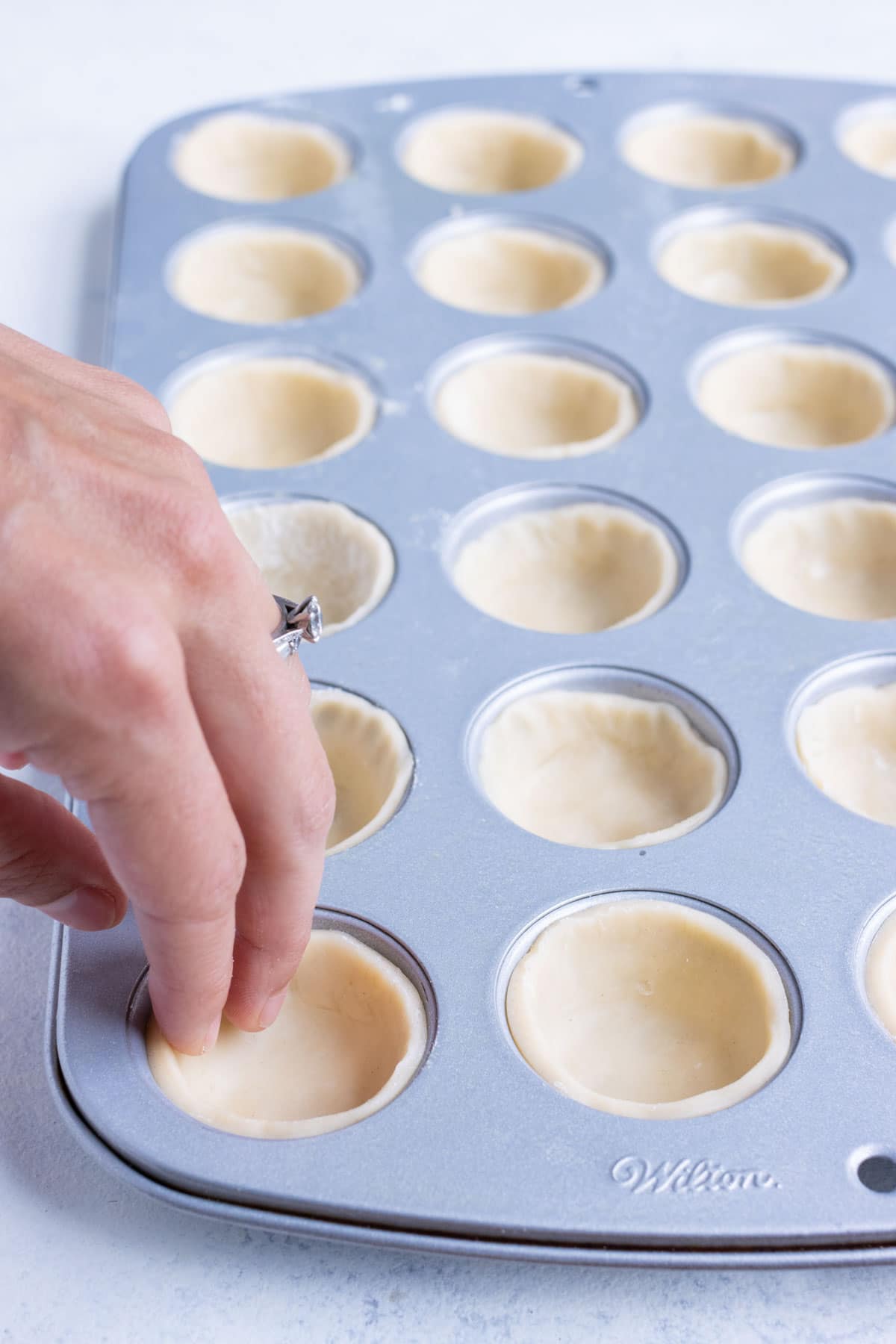 Pie crust is pressed into a mini muffin pan.