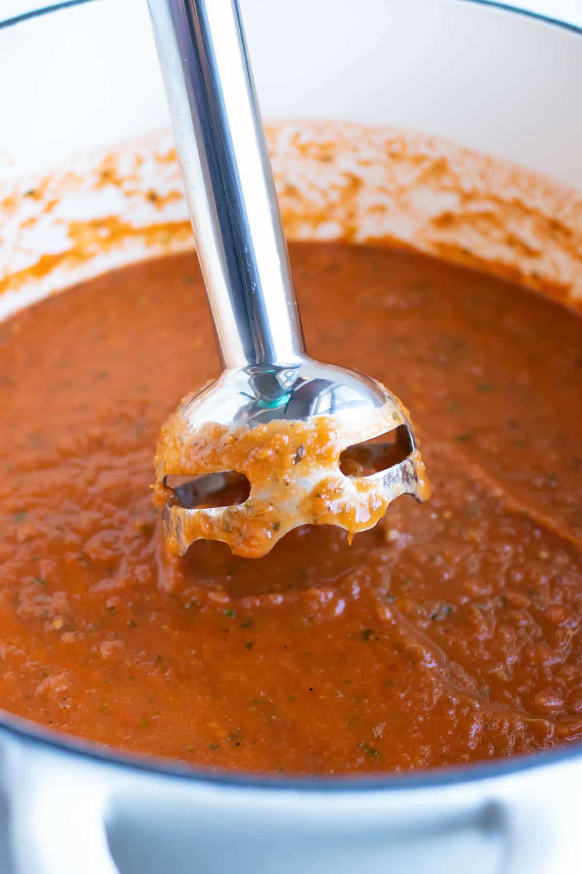 An immersion blender coming out of a pot of tomato basil soup.