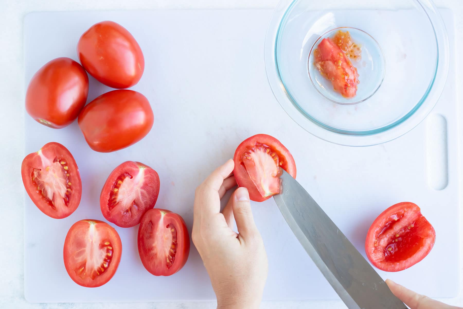 A hand deseeding a tomato with a knife.