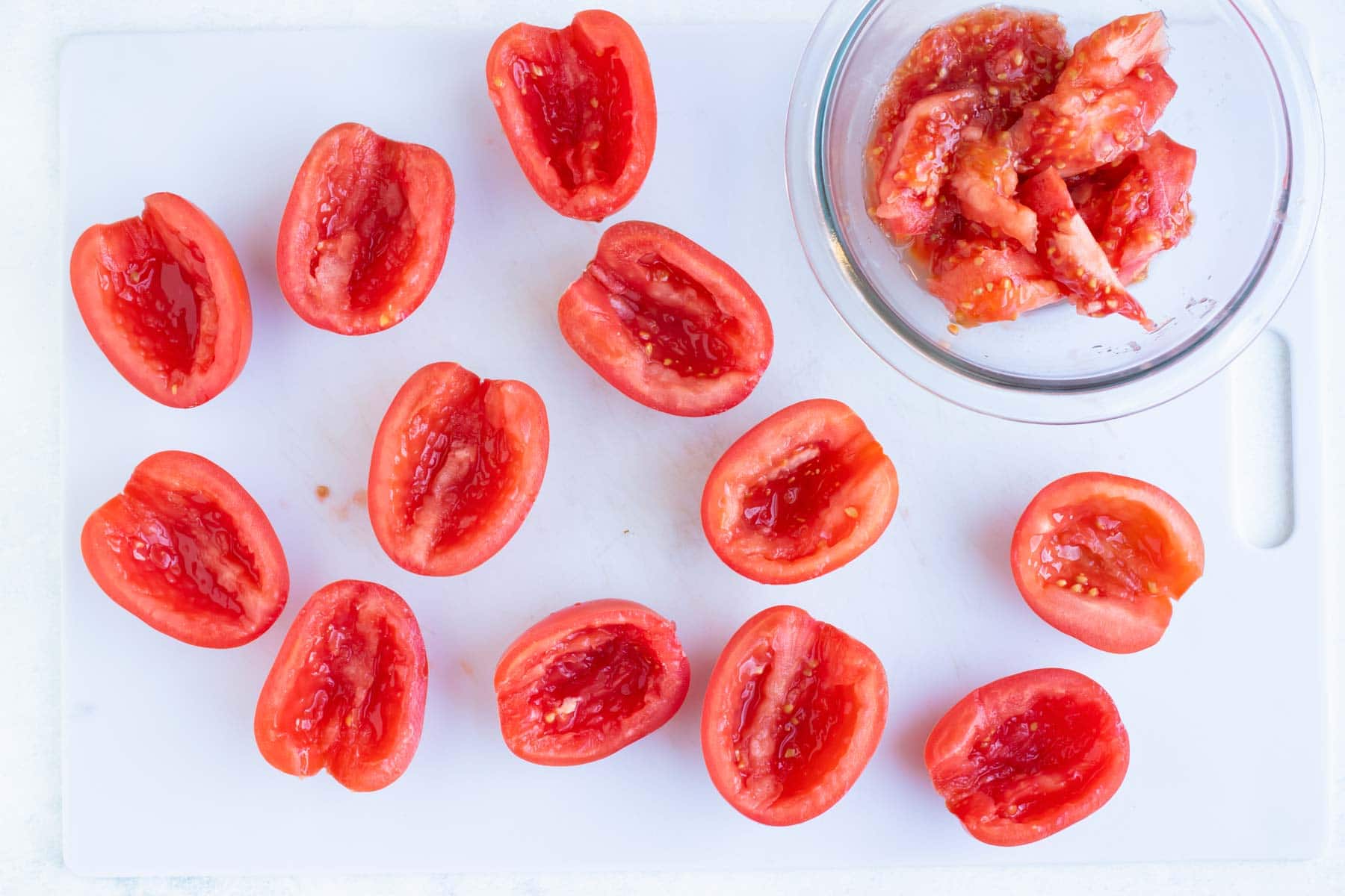 Halved and deseeded tomatoes on a white cutting board.