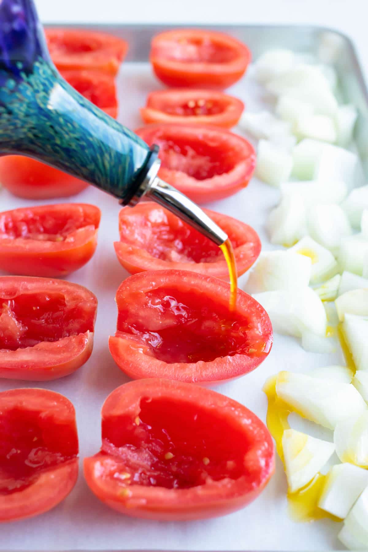 Pouring olive oil over tomatoes and onions to be roasted in the oven.