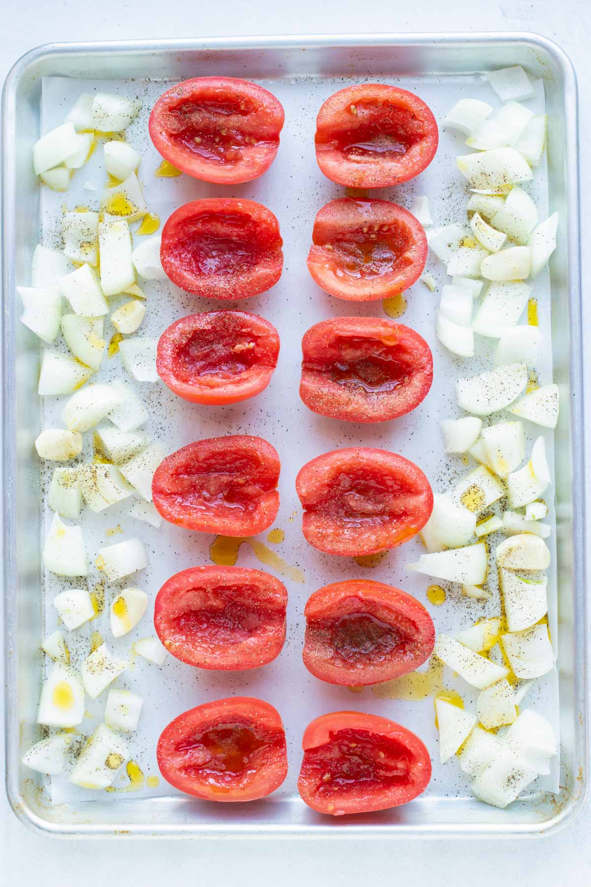 Olive oil coats tomatoes and onions to be roasted in the oven.