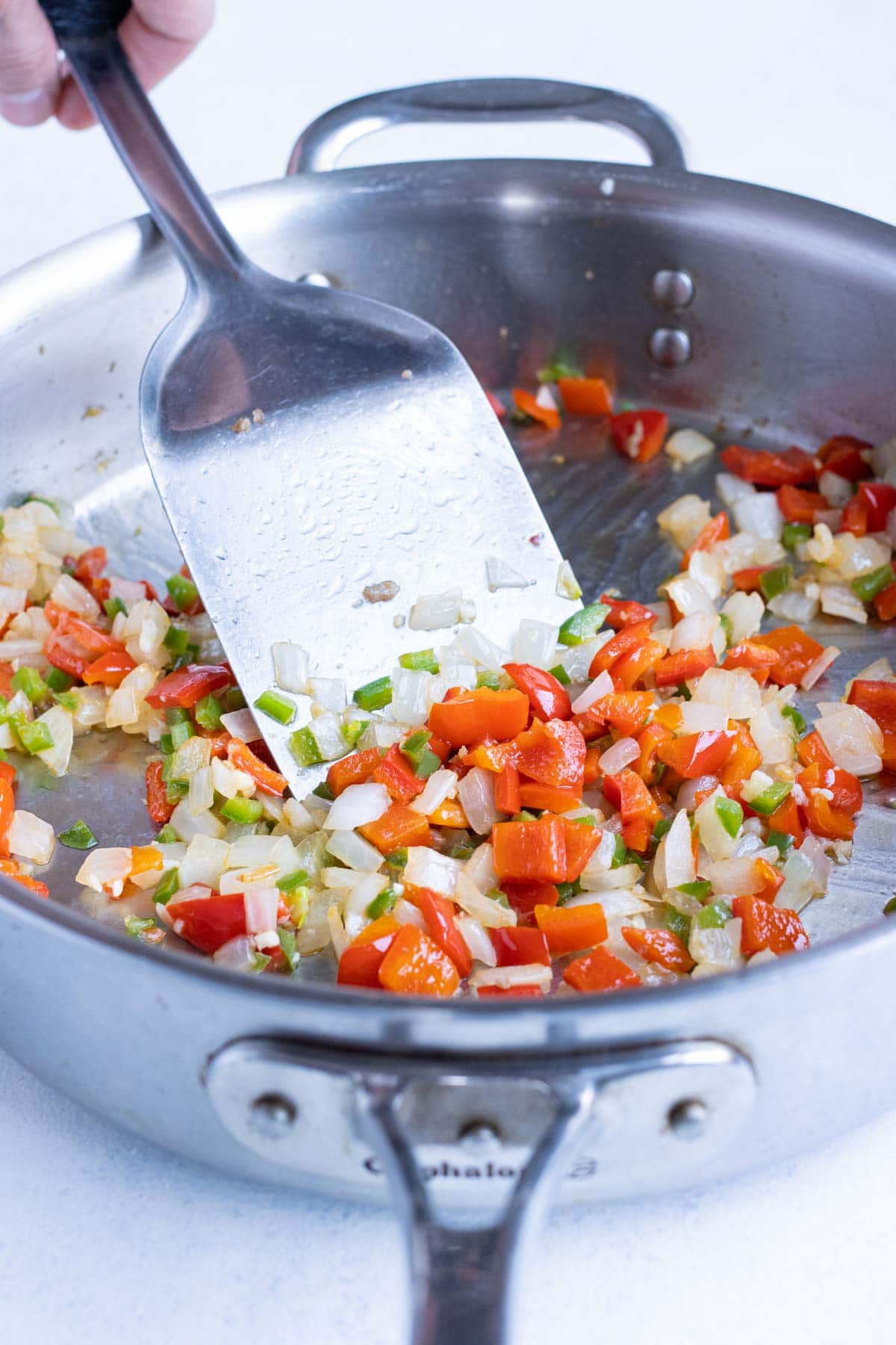 Diced onions and peppers are sautéd on the stove.