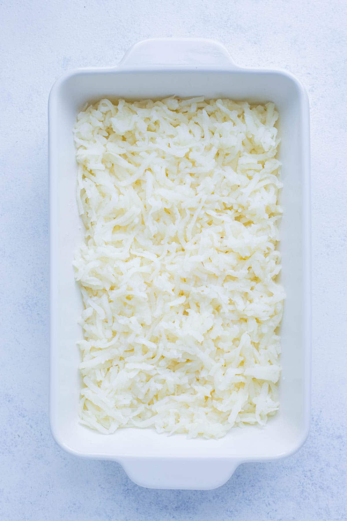 Hashbrowns are laid first in a baking dish.