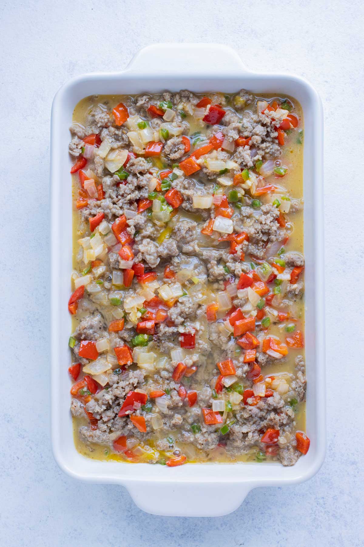 Cooked sausage, bell peppers, and eggs are layered on top of the hashbrowns.