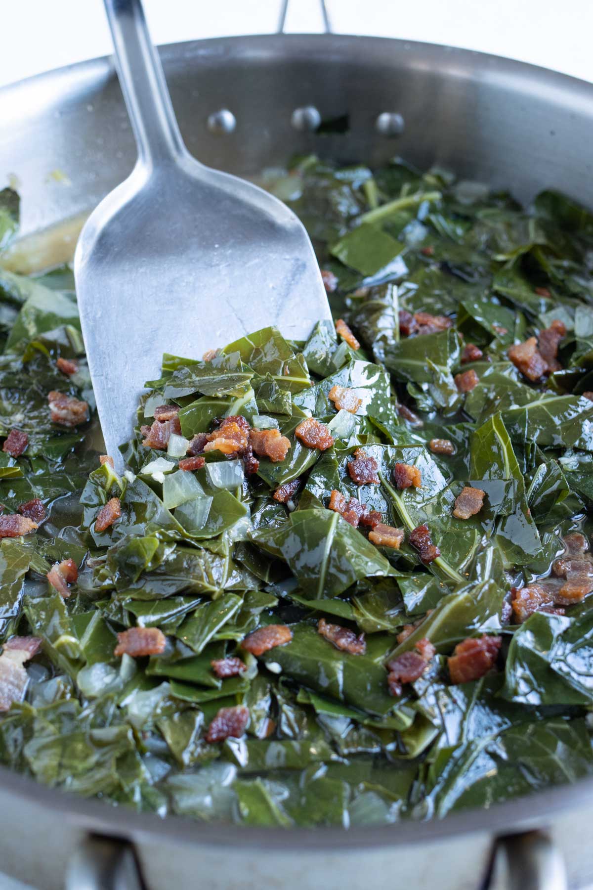 A pan in shown with cooked southern collard greens and bacon.