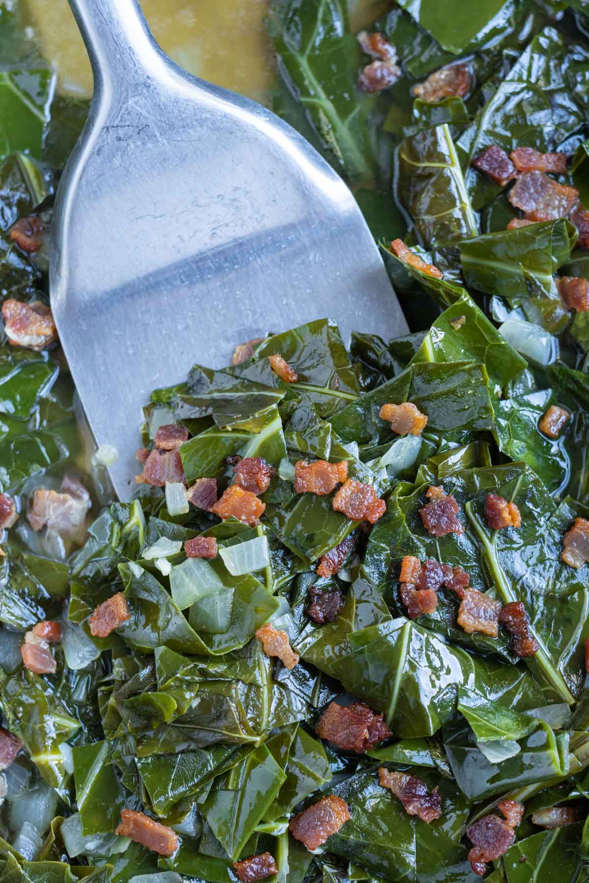A spatula is shown dishing the collard greens from a pan.
