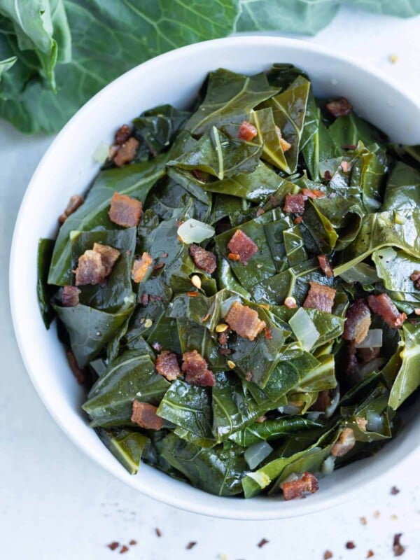 Southern collard greens with bacon are served in a white bowl with onions.