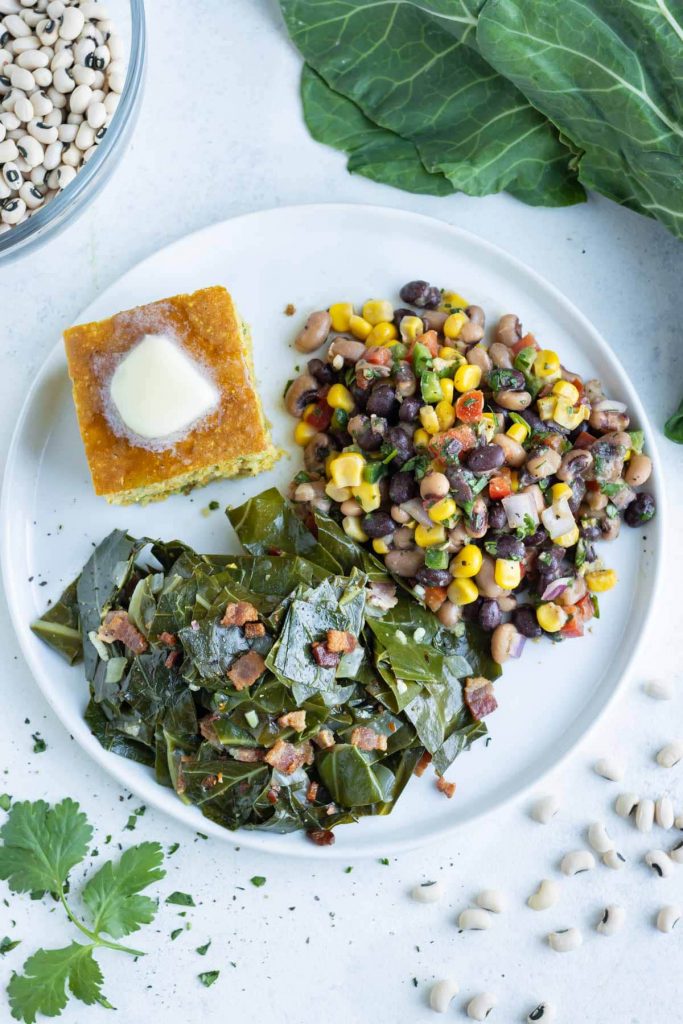 A plate is shown on the counter with collard greens, Texas caviar, and corn bread.