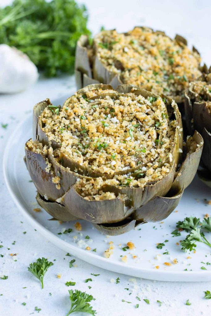 Golden and tender stuffed artichokes are served on a white plate.