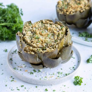 A white plate is used to serve stuffed artichokes.