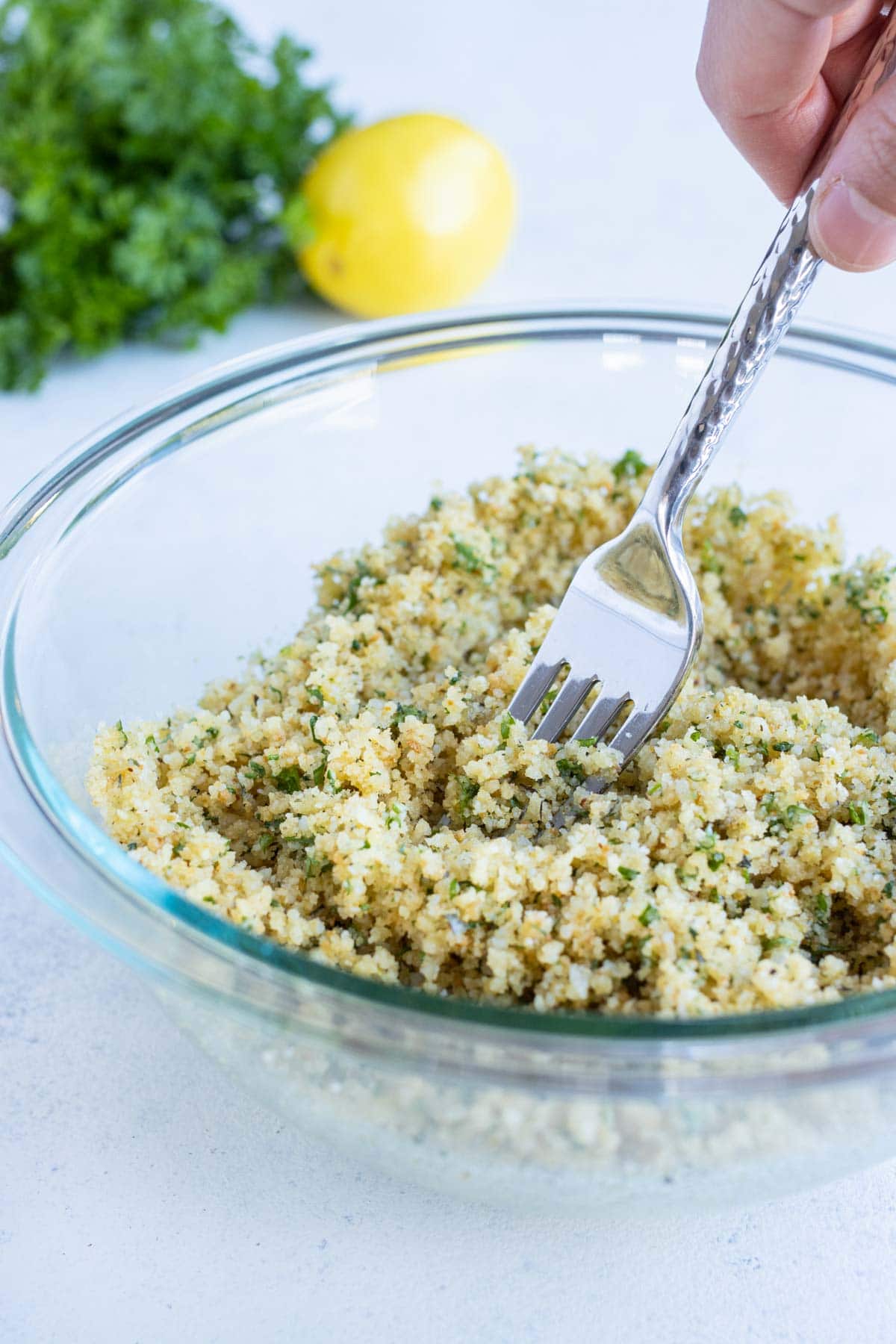 Breadcrumbs are combined with Parmesan cheese, parsley, salt, pepper, zest, and oil in a bowl.