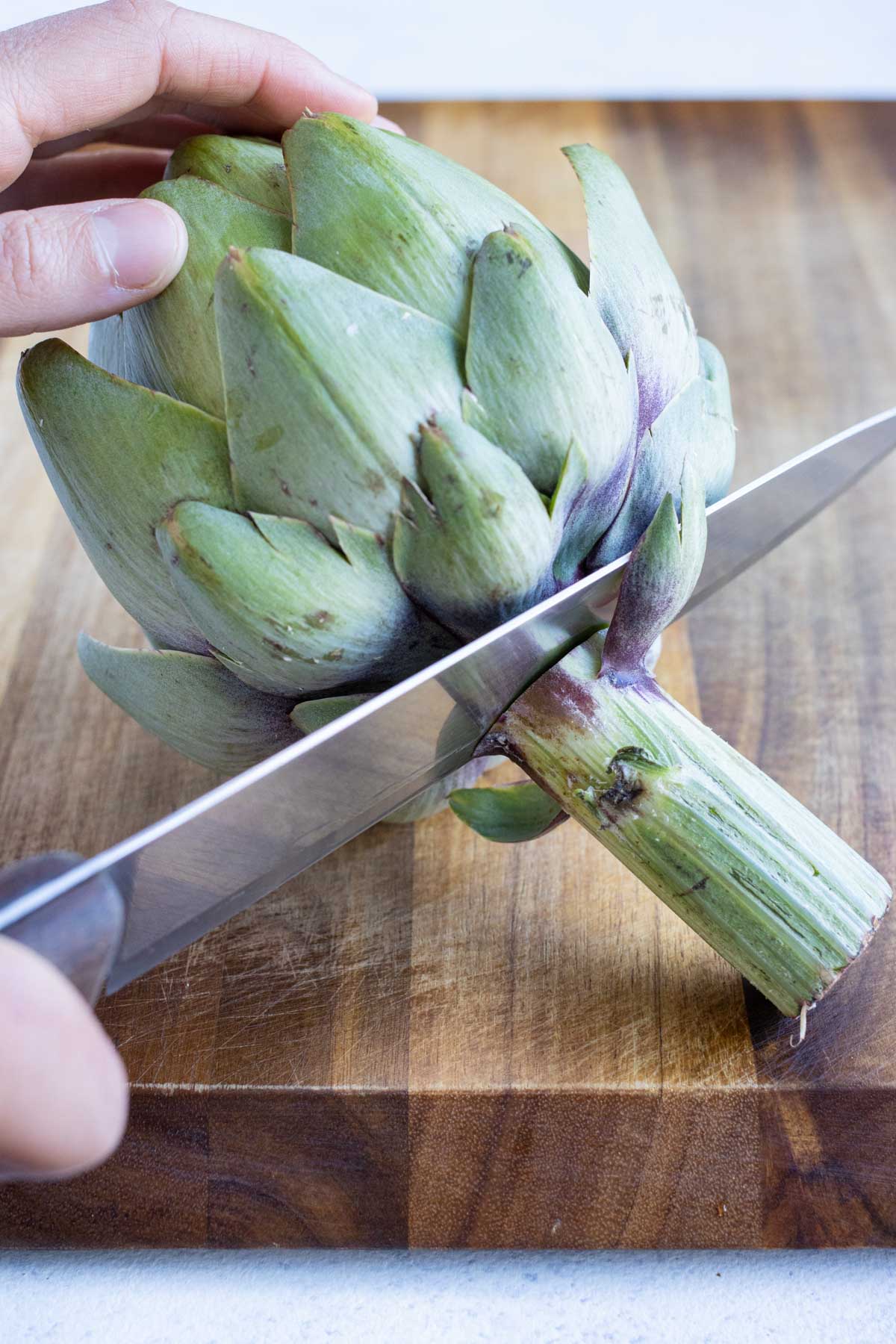The stem is trimmed from the artichoke.