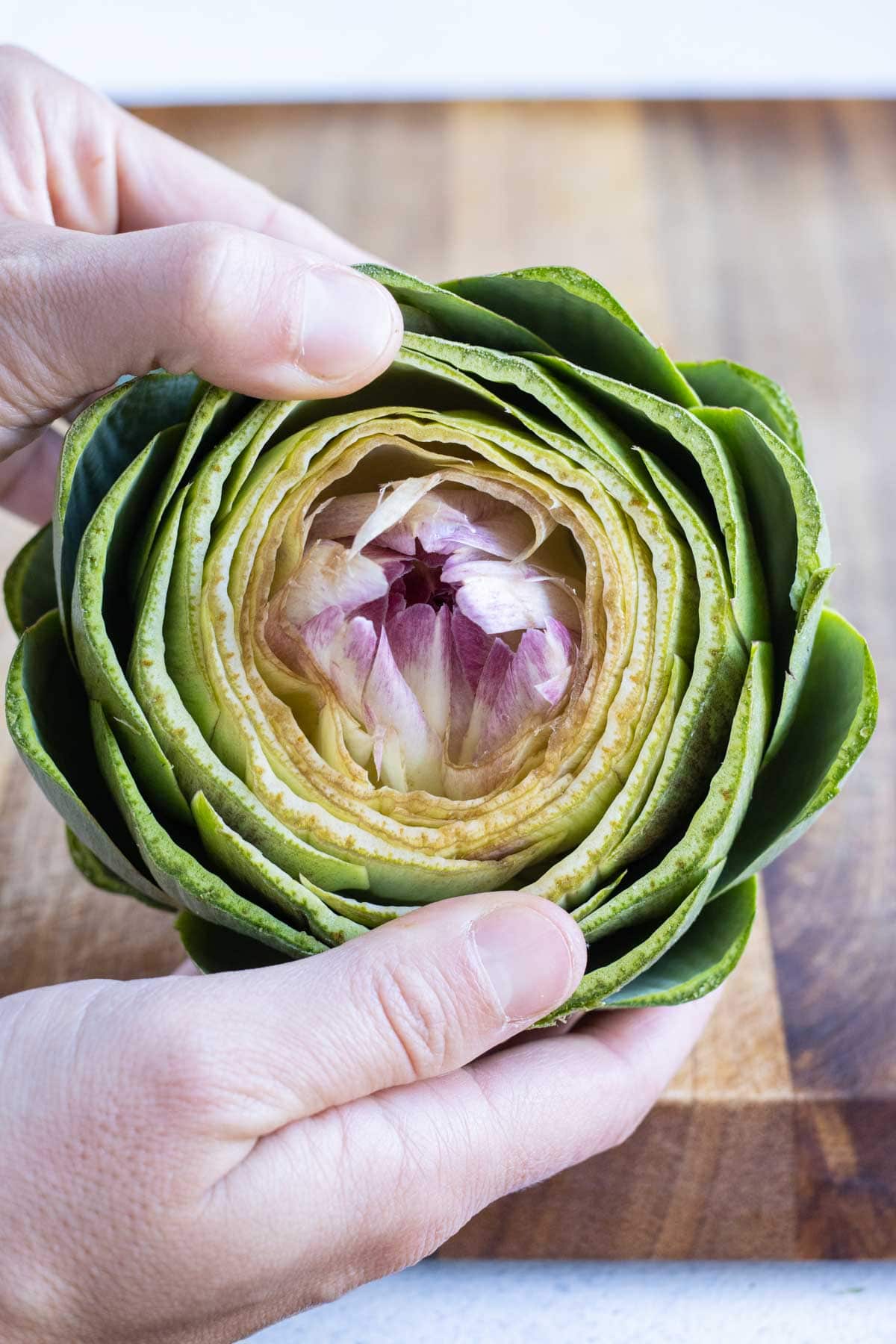 Both hands are used to pry apart the artichoke until you see the heart.