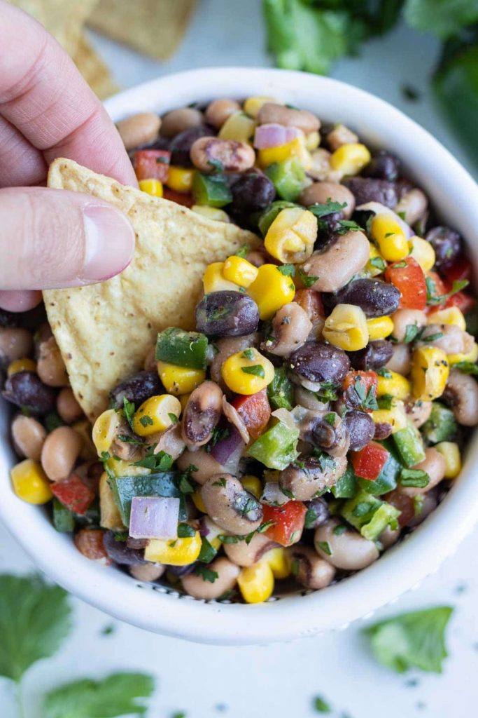 A hand is dipping a chip into the Texas caviar dip.