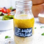 A glass bottle of a homemade remake of Olive Garden Italian Dressing recipe is on a table.