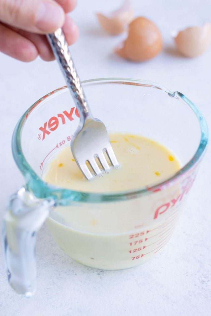 Egg and milk are whisked together in a measuring cup.