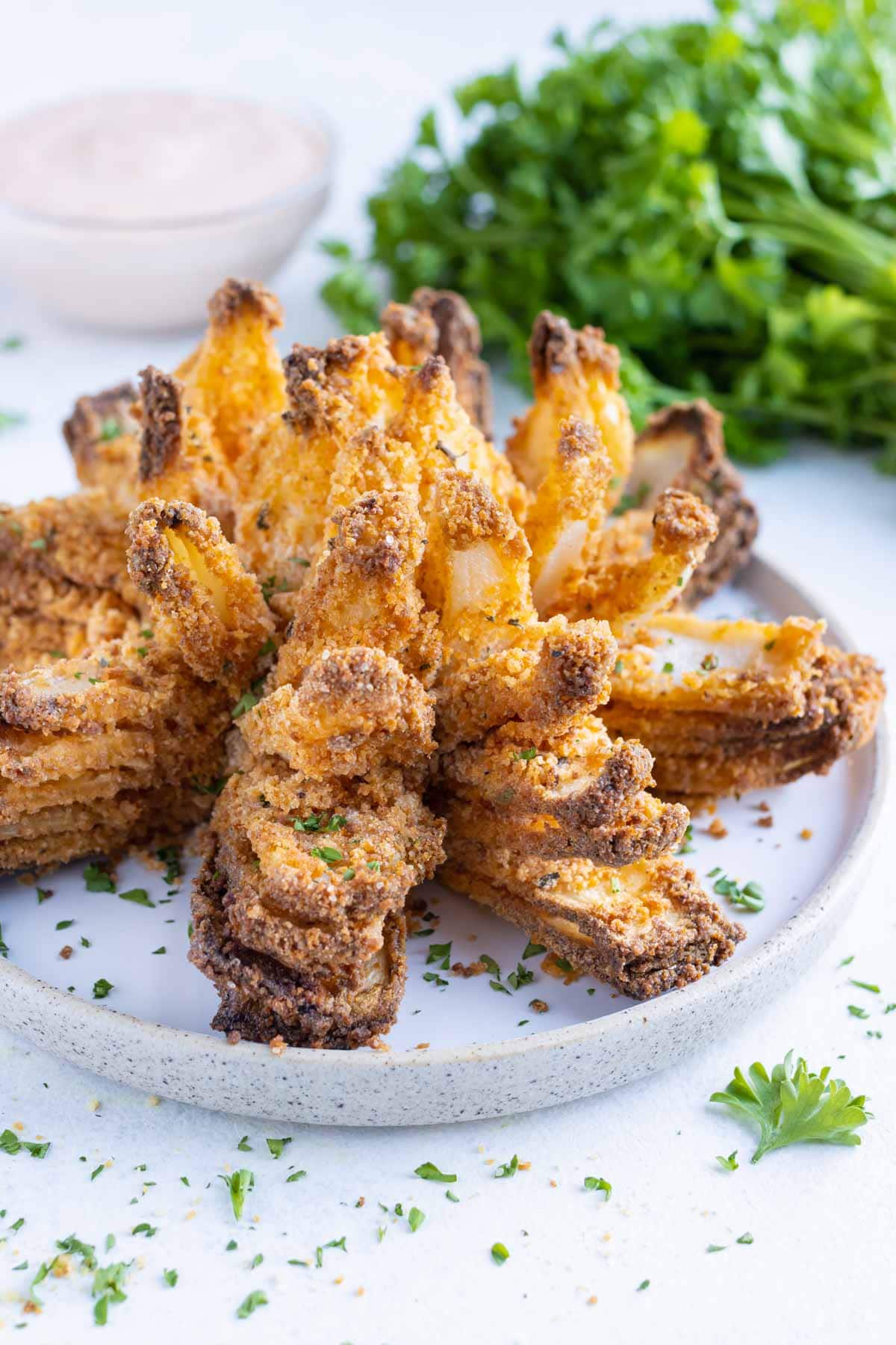 Fried blooming onion is topped with fresh parsley and plated for an appetizer.