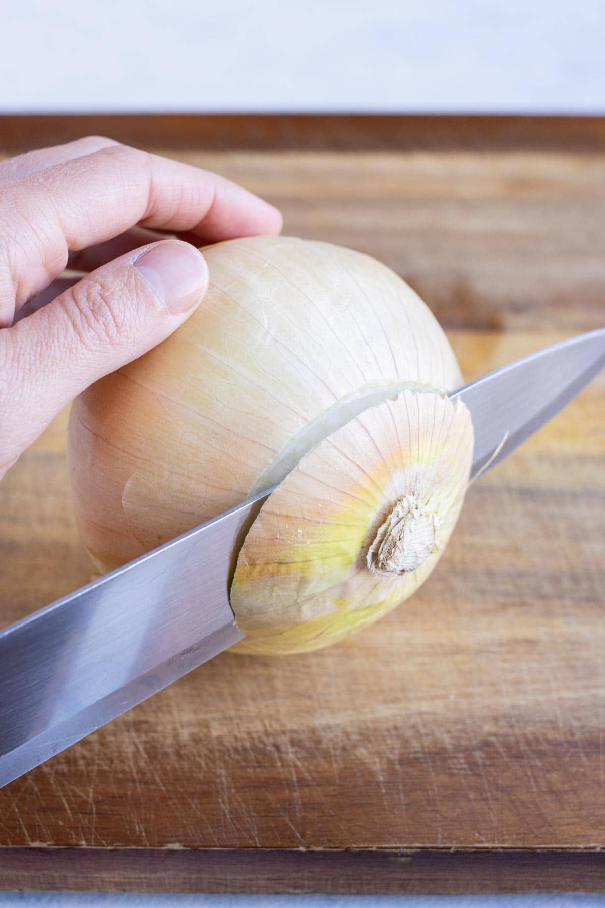 The top of the onion is cut off with a knife.