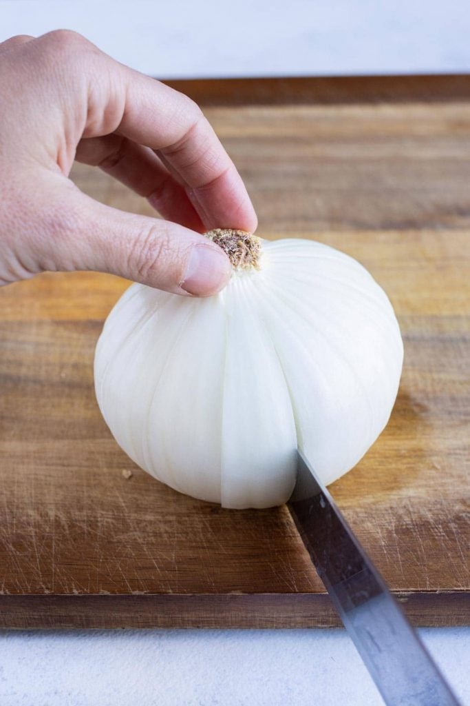 A knife cutting the onion into petals for an air fryer blooming onion.
