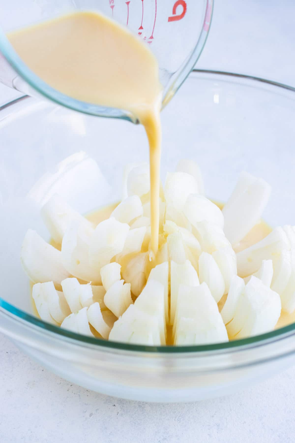 Cut onion in a bowl is covered in the milk and egg mixture.