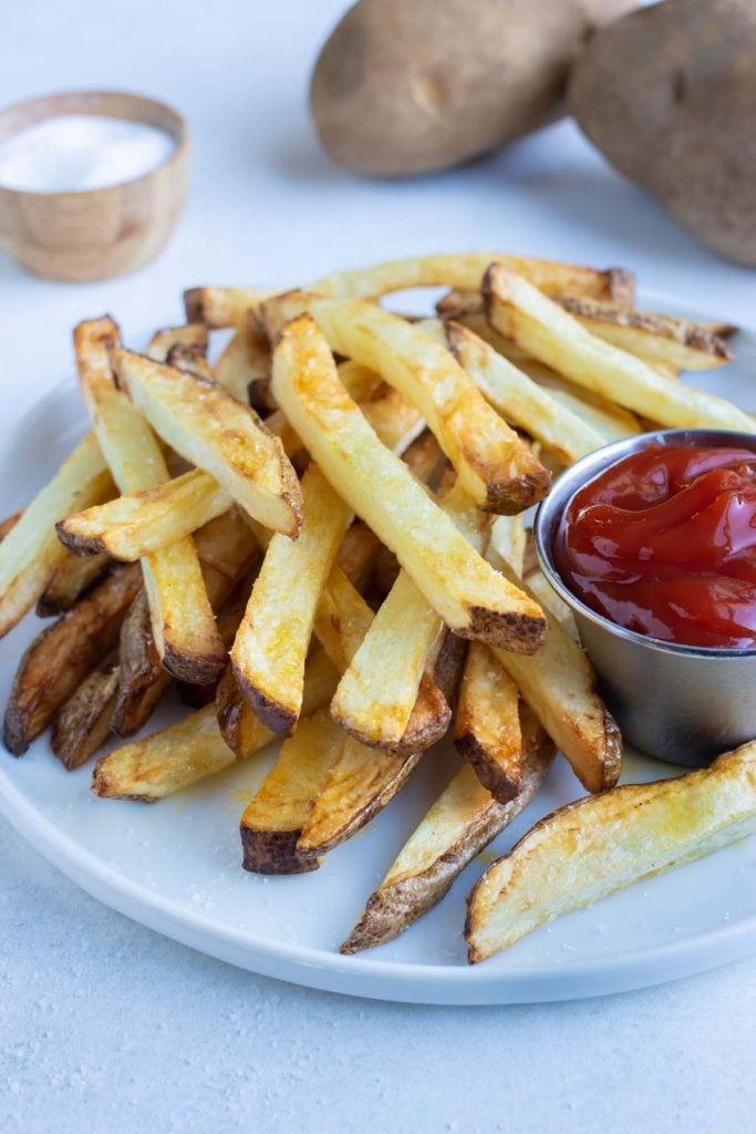 A pile of air fryer french fries are shown on a white plate on the counter.